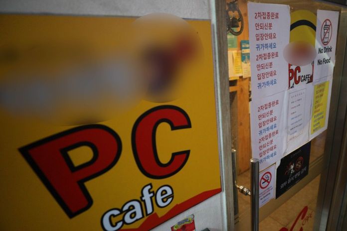 Entrance to a PC cafe featuring signs that include 'No Drink No Food' and various messages in Korean regarding entry rules.