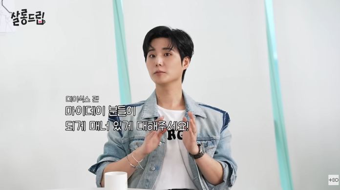 Young K in a denim jacket gestures while speaking, with text in Korean overlaying the image.