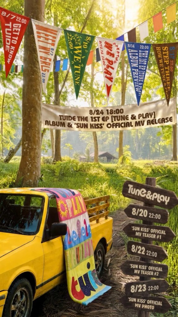 Colorful event banners hanging in a forest setting promoting the release of an album titled 'Tune & Play' and its music video 'Sun Kiss', with a yellow truck and a vibrant blanket draped on it.