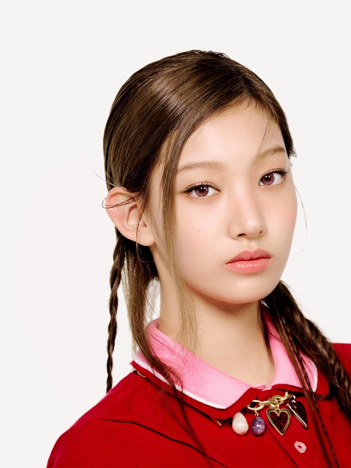 Seoyeon with long, smooth hair, styled with braids, wearing a red shirt with a pink collar and a decorative necklace featuring charms. The background is plain white, emphasizing their facial features and expression.