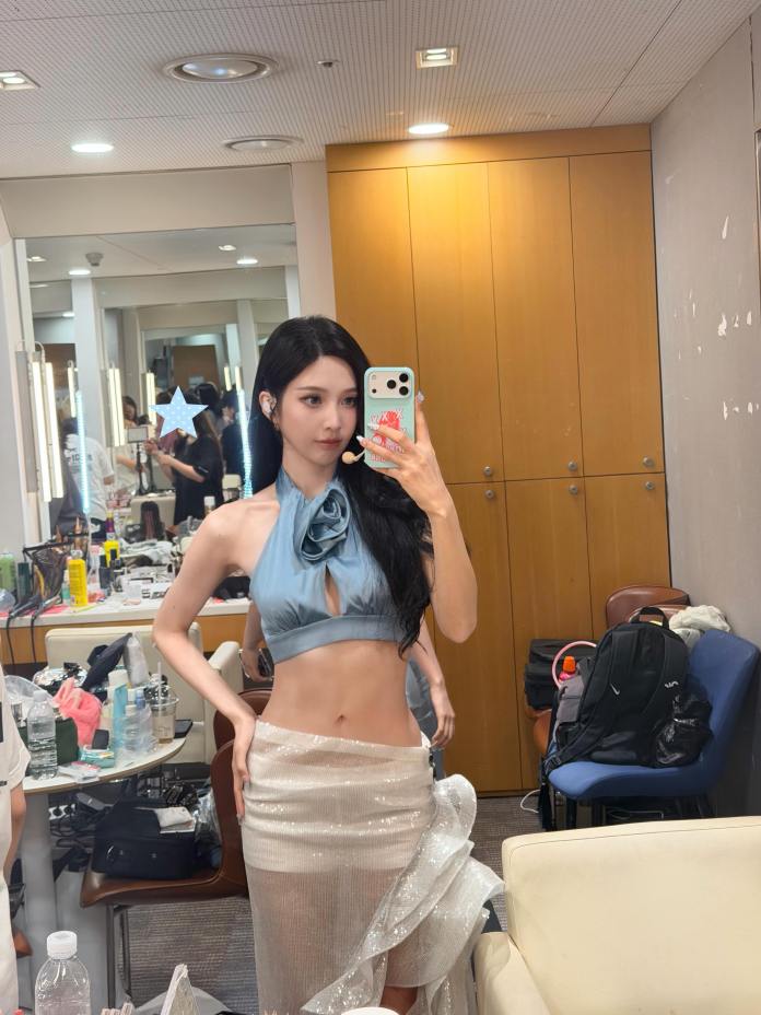 Joy posing in front of a mirror wearing a stylish blue halter top and a shimmering skirt, showcasing her outfit in a dressing room.