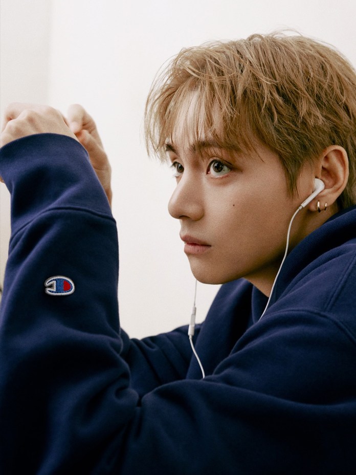 Profile view of BTS V with light brown hair wearing a navy sweatshirt with earbuds in their ears, gazing thoughtfully.