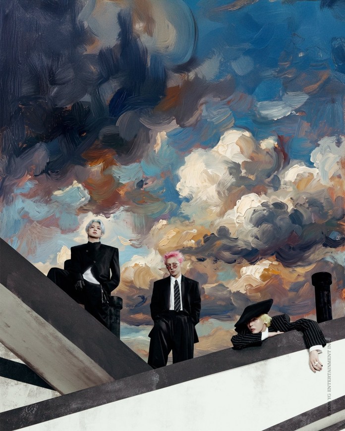 Three individuals in stylish black suits pose on a dramatic architectural structure against a colorful, cloudy sky.