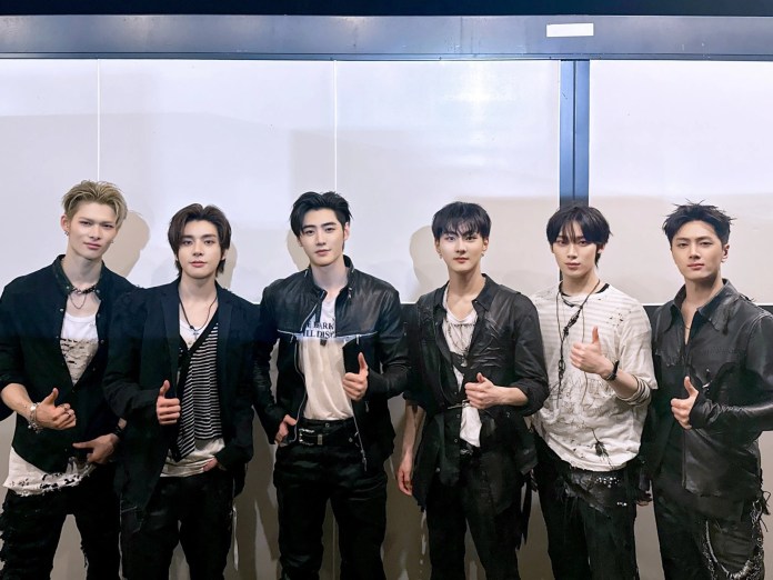 ENHYPEN members posing together in stylish black outfits, with a mix of casual and edgy fashion elements. They are standing in front of a white background, each showing a thumbs-up gesture.