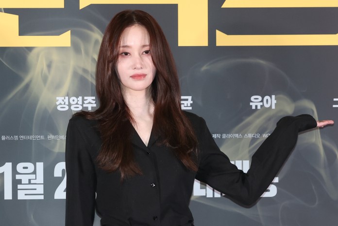 Jeon Jong-seo with long dark hair wearing a black outfit poses with one hand raised against a background featuring text in Korean.
