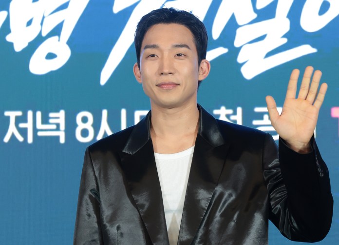 Lee Sang-yi in a black blazer and white shirt smiling and waving at an event.