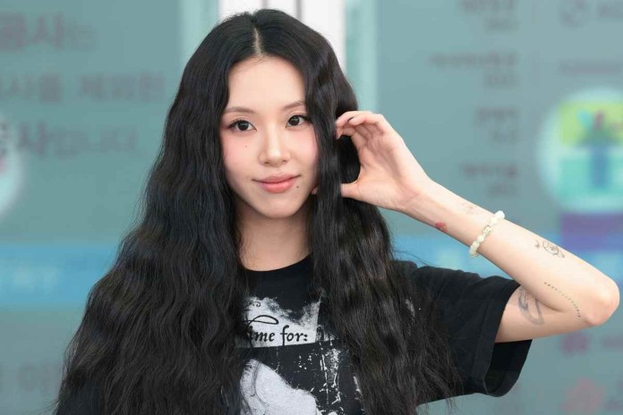 Chaeyoung with long, wavy black hair wearing a graphic black t-shirt, smiling and touching her hair with one hand.