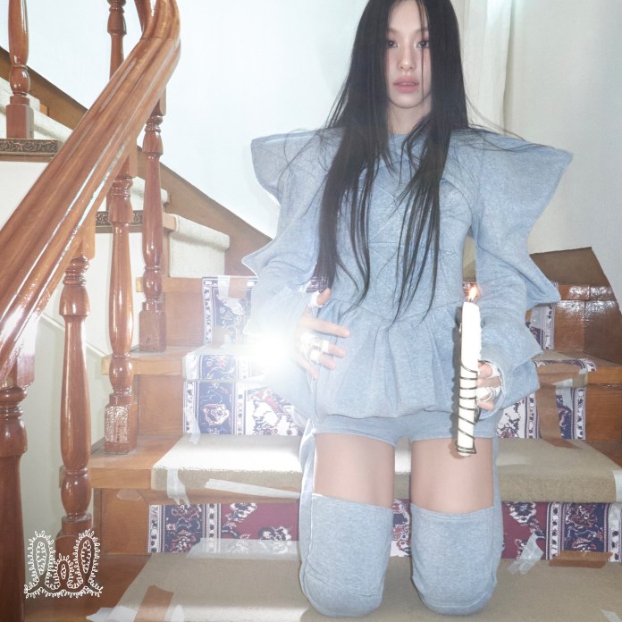Chaeyoung wearing a gray oversized outfit kneeling on the stairs, holding a lit candle, with long dark hair and a solemn expression.