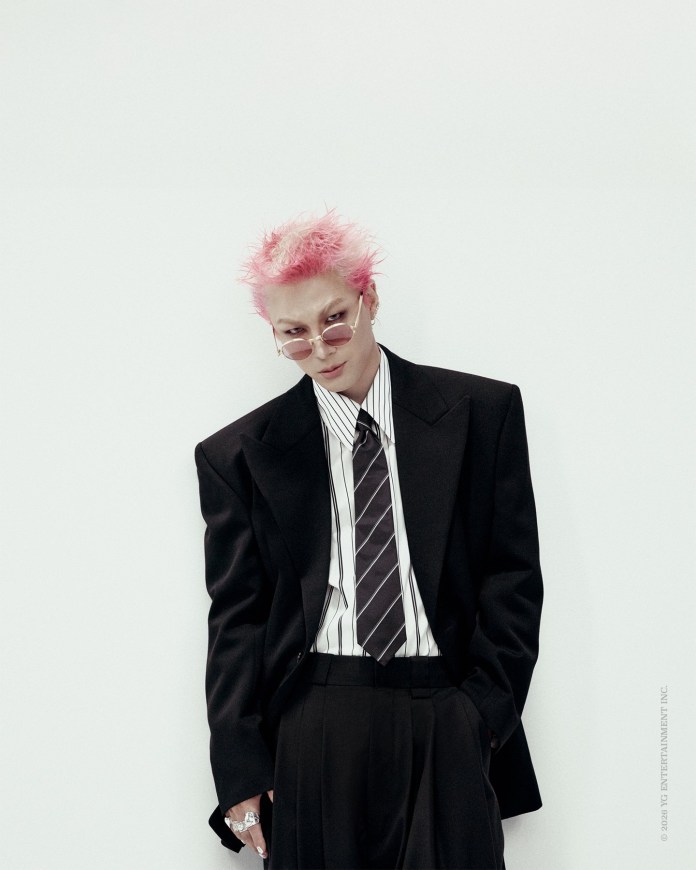 Taeyang with pink spiky hair wearing sunglasses, a black oversized blazer, and a striped shirt with a tie, standing against a white background.