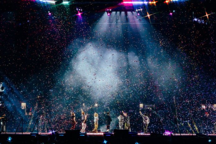 A colorful stage performance with BTS silhouetted against a backdrop of confetti and bright stage lights.