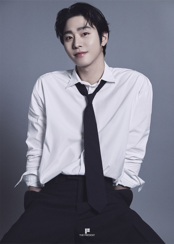Ahn Hyo-seop wearing a white shirt and black tie, smiling and posing casually against a gray background.