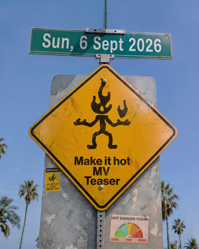 A traffic sign on a pole indicating 'Make it hot MV Teaser' with a cartoonish figure engulfed in flames. It also features a date 'Sun, 6 Sept 2026' at the top and a fire danger indicator below, accompanied by palm trees in the background.