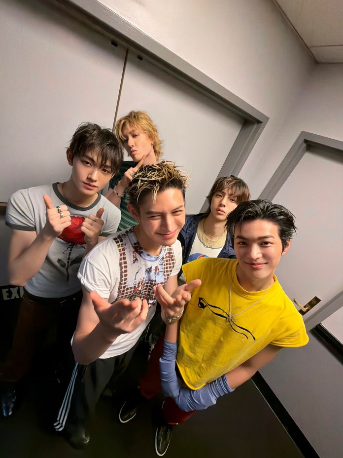 CORTIS members posing together in a narrow hallway, showing playful expressions and a mix of casual clothing styles.