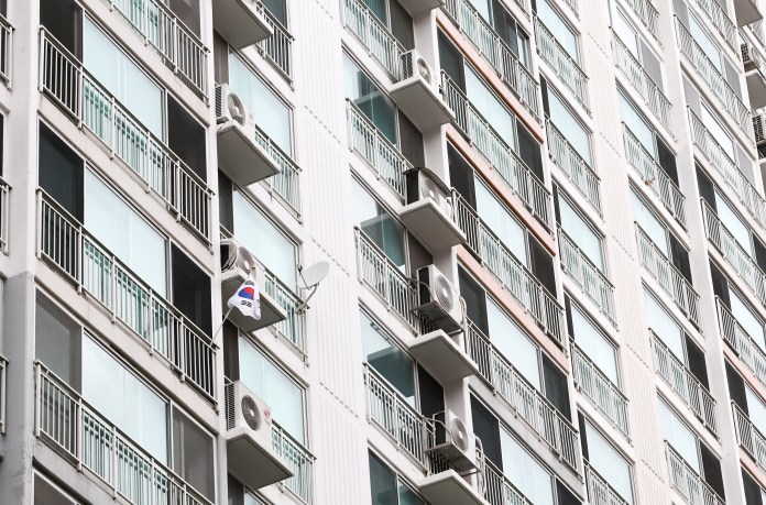 A close-up view of a residential building facade featuring multiple balconies and air conditioning units, with a small flag displayed from one balcony.