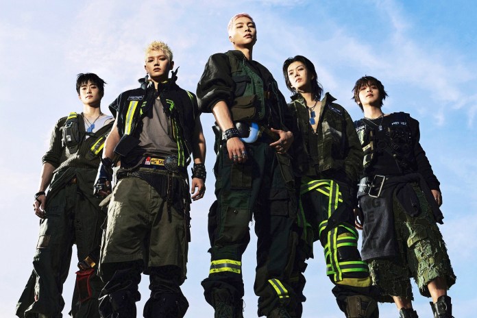 NCT wearing futuristic military-inspired outfits, posing confidently against a blue sky.