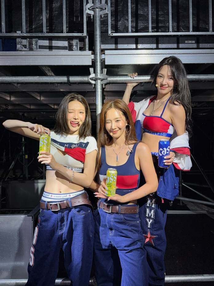 Sooyoung, Hyoyeon, and Yuri posing together in casual outfits, holding beverages, with a stage backdrop.