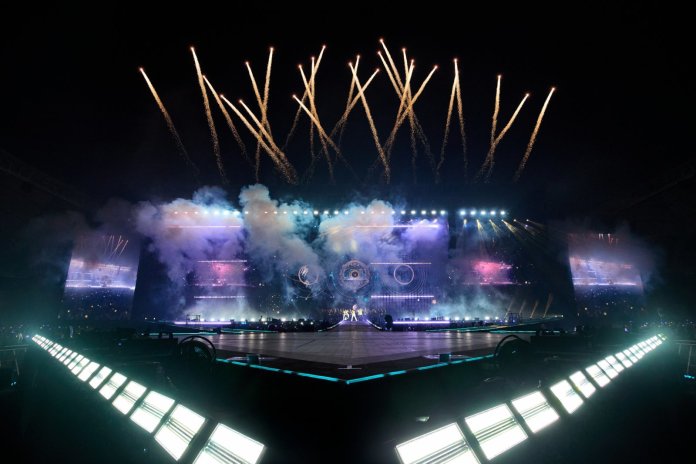 BIGBANG with colorful lights and smoke, featuring fireworks erupting in the night sky.