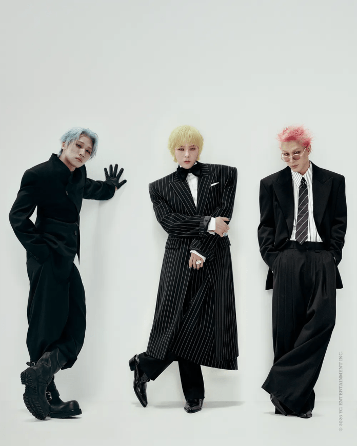 Three stylish individuals posing against a plain background, showcasing unique hairstyles and fashionable outfits. The person on the left has blue hair and a black ensemble, the center figure sports a yellow hairstyle and a pinstriped formal outfit, while the person on the right features pink hair and a formal black suit.