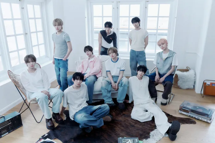 AHOF posing indoors, wearing casual outfits in light colors. They are arranged in two rows with a cozy, bright background featuring large windows and wooden flooring.