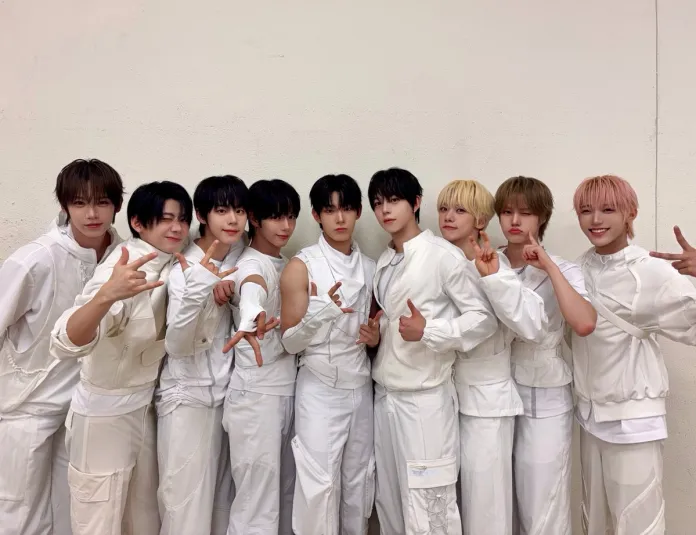 AHOF posing together in matching white outfits, some making playful gestures and smiling, against a plain background.