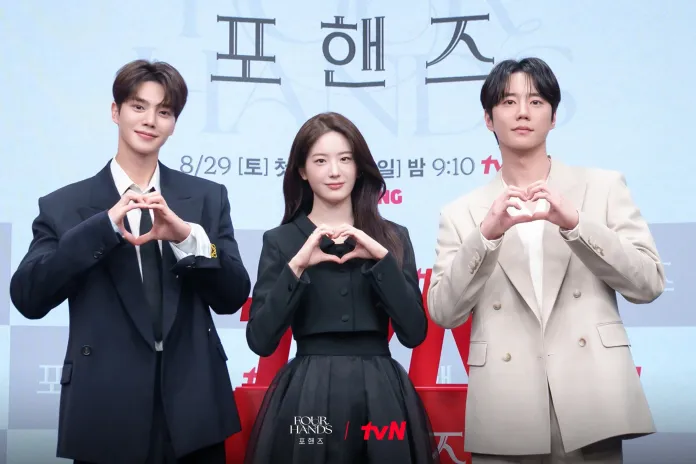 Song Kang Jang Gyuri and Lee Jun-young forming heart shapes with their hands, posing at a promotional event for the show 'Four Hands'.