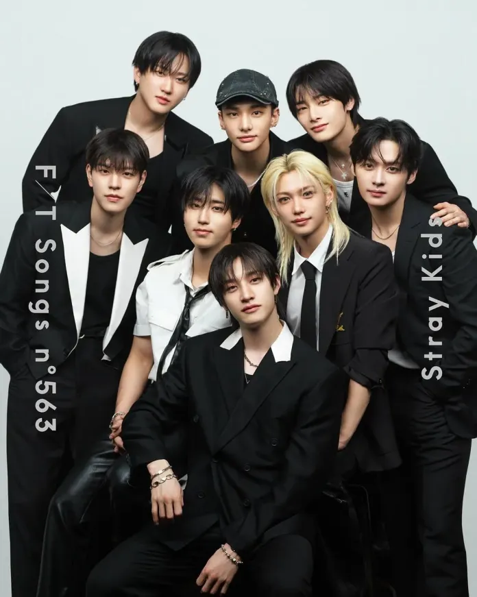 A group photo of eight male members of a music group posing together, dressed in stylish black and white outfits against a plain background.