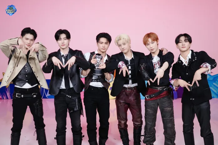 A group of six men posing together, each making hand gestures while dressed in stylish outfits with a colorful background.