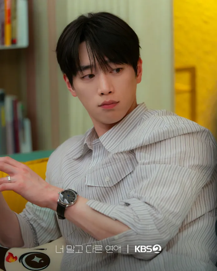 Seo Kang Joon wearing a striped shirt and a watch, looking thoughtfully to the side while seated on a couch.