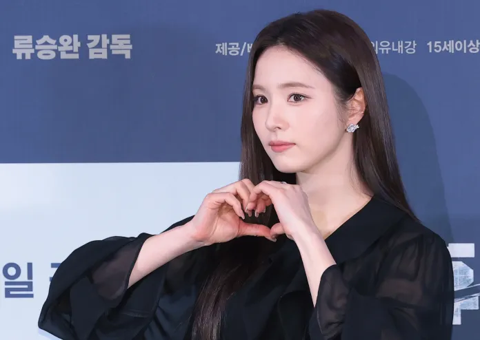  Shin Se Kyung in a black outfit makes a heart shape with her hands, posing for the camera at a promotional event.