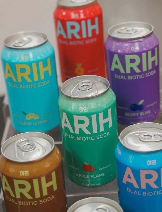 Colorful cans of ARIH dual biotic soda labeled with different flavors including Clear Lemon, Apple Flare, and Berry Bliss.