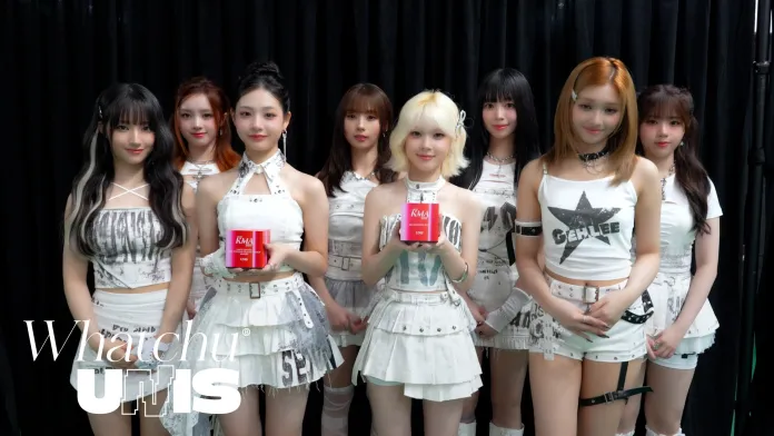 UNIS posing together, all wearing coordinated white outfits with black accents. The central figure holds a red product, while the others stand closely around her, smiling at the camera.