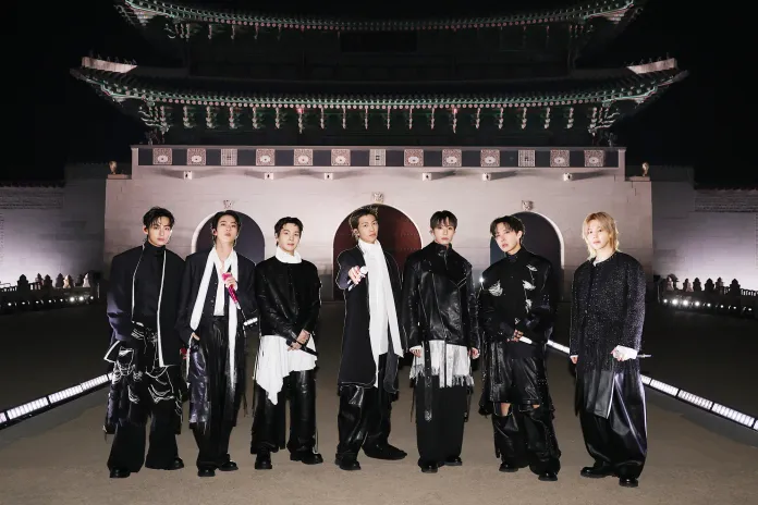 BTS members dressed in stylish black outfits with white accents, posing confidently in front of a traditional Korean structure at night.