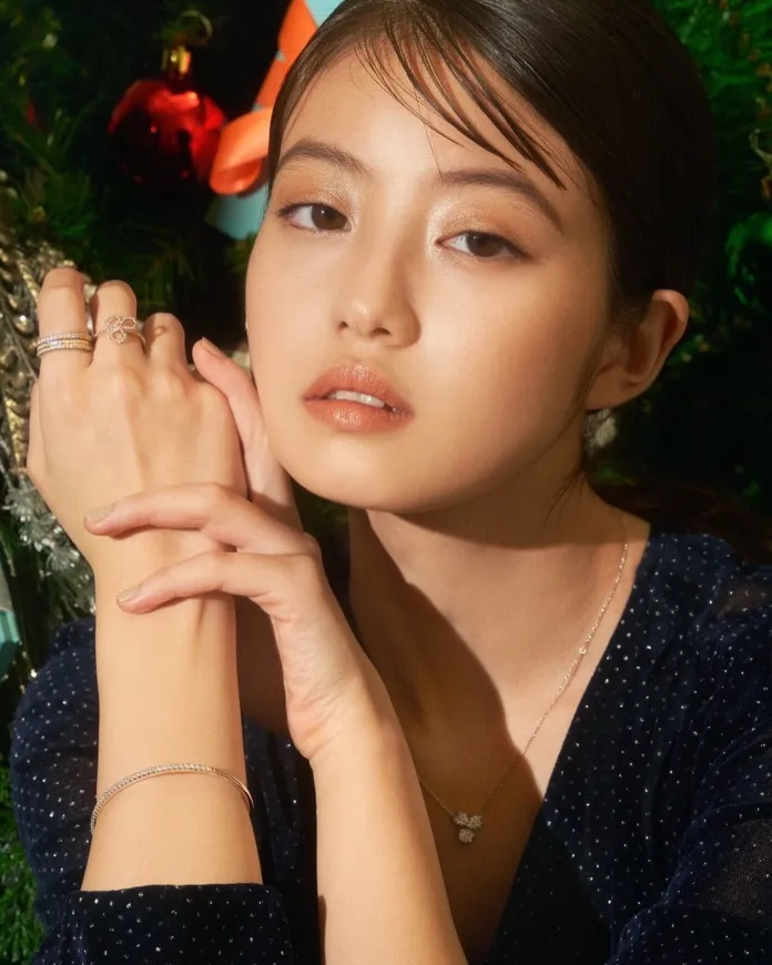 Close-up portrait of Imada Mio with elegant jewelry, including rings and a necklace, posed against a festive background with Christmas decorations.