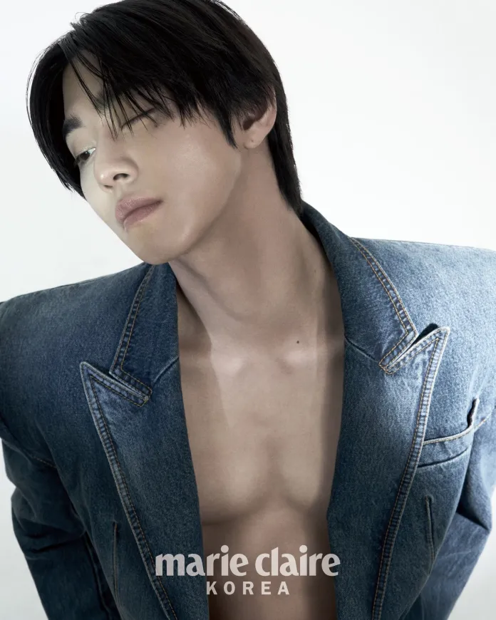 A close-up portrait of a person wearing a denim jacket, with a serious expression and slightly tilted head, showcasing their collarbone and neck against a plain white background.
