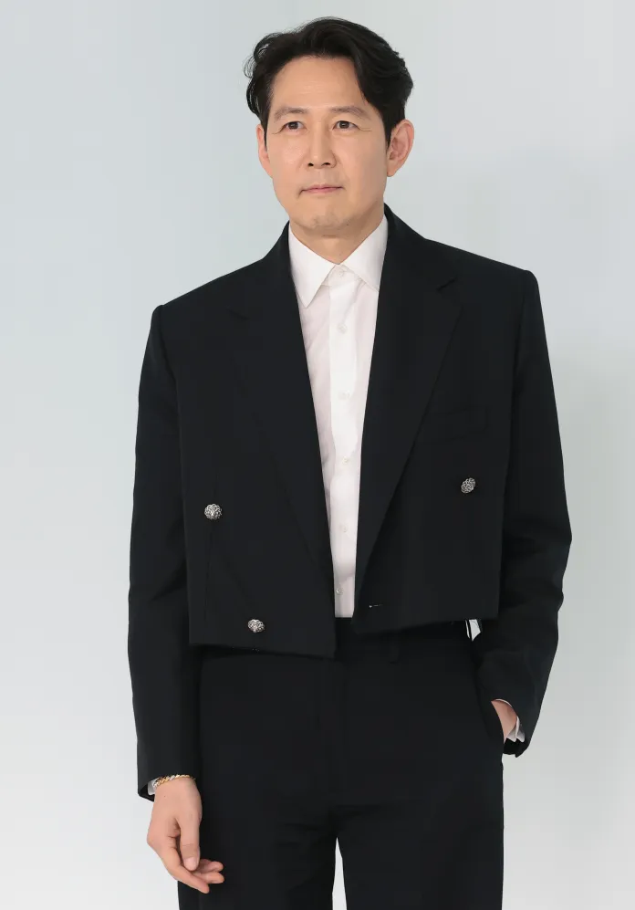 Lee Jung-jae in a stylish cropped black suit jacket over a white shirt, posed against a light background.