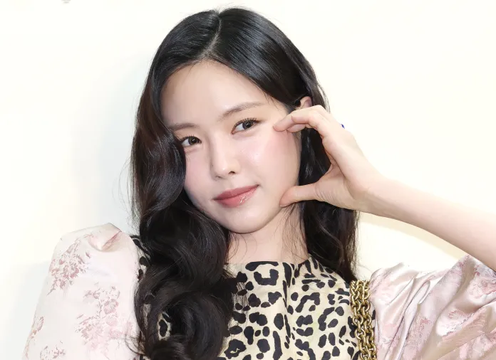 Close-up portrait Son Naeun with long dark hair, wearing a leopard-print top and making a playful gesture with her hand near her face.