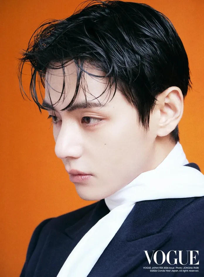 V with slicked-back hair and a white scarf, against an orange background.