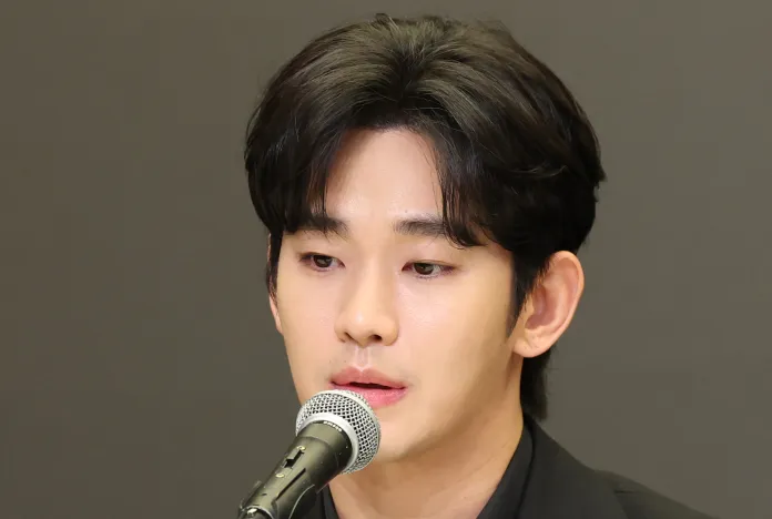 Close-up of a man speaking into a microphone, with black hair and a serious expression, against a dark background.