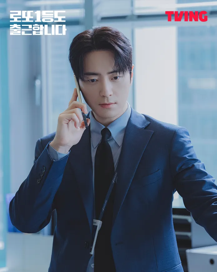 Lee Joon-hyuk in a blue suit talking on a smartphone in an office setting, appearing focused and engaged.