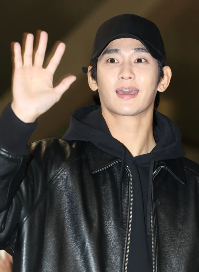 Kim Soo-hyun wearing a black cap and leather jacket waves and smiles, showcasing a friendly demeanor.