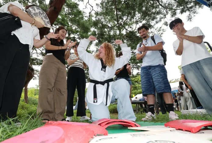 A group of people cheer and celebrate around a woman in a karate uniform demonstrating strength and confidence outdoors.