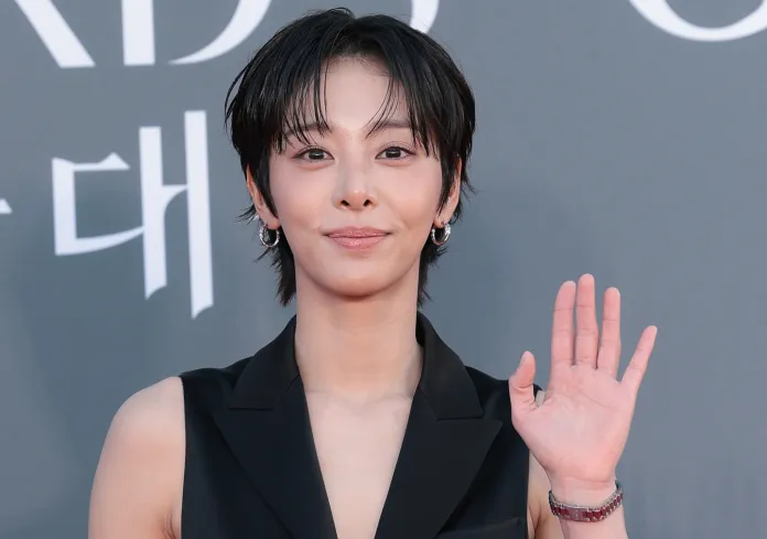 Seol In-ah with short black hair and earrings, wearing a black outfit, smiling and waving at the camera at a public event.