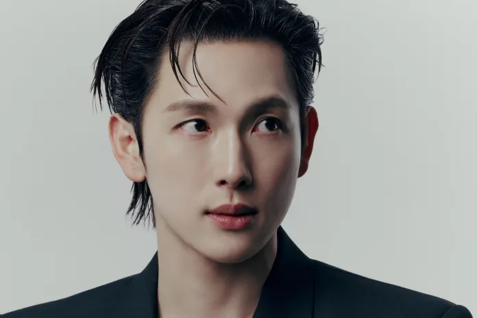 Close-up portrait of Im Siwan with slicked-back hair, wearing a black suit, gazing to the side against a light background.