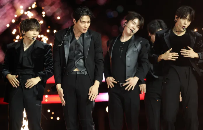 THE BOYZ in stylish black outfits, dancing on stage with dramatic lighting and sparkles in the background.