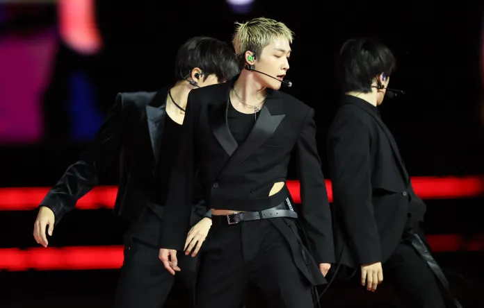 THE BOYZ in black outfits, showcasing a dynamic dance pose on stage, with colorful lights in the background.