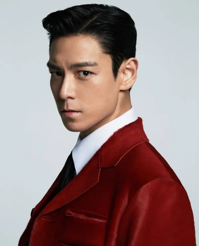 T.O.P wearing a red suit jacket, looking confidently to the side with a serious expression against a plain background.