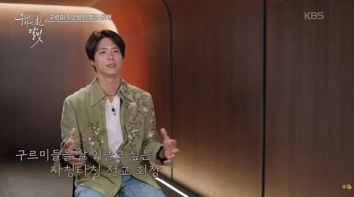 Park Bo Gum with dark hair and a green floral shirt sitting in a modern interior, gesturing with his hands while speaking during an interview.