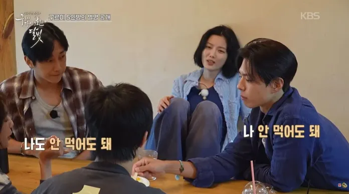 Park Bo Gum sitting at a wooden table, engaged in a conversation. 