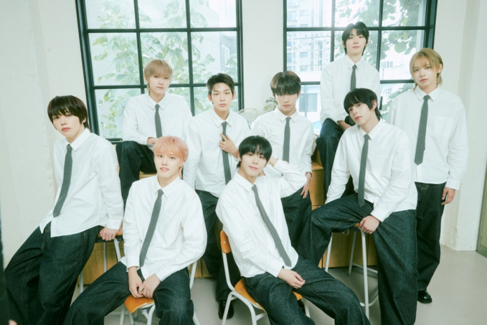 A group of ten individuals in formal attire, wearing white shirts and black ties, posing in a bright room with large windows. They are seated and standing around a mix of chairs and a table.