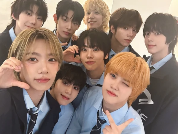 A group selfie featuring nine young men posing together with smiles and playful expressions, all dressed in light blue shirts with ties.